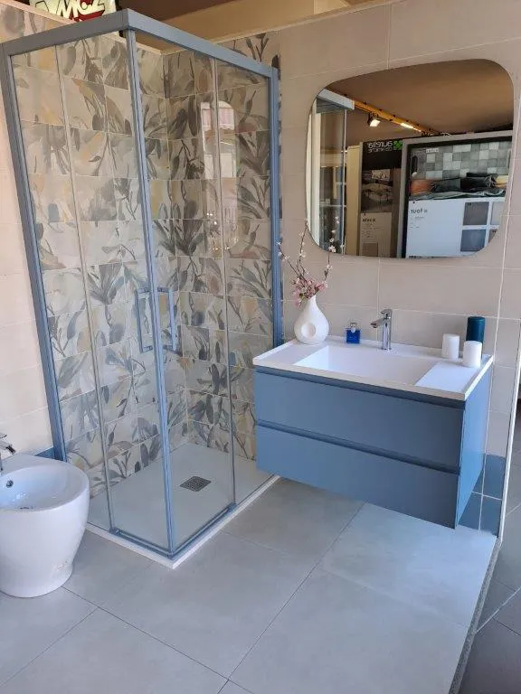 Bagno con box doccia, rivestimento floreale e mobile sospeso blu