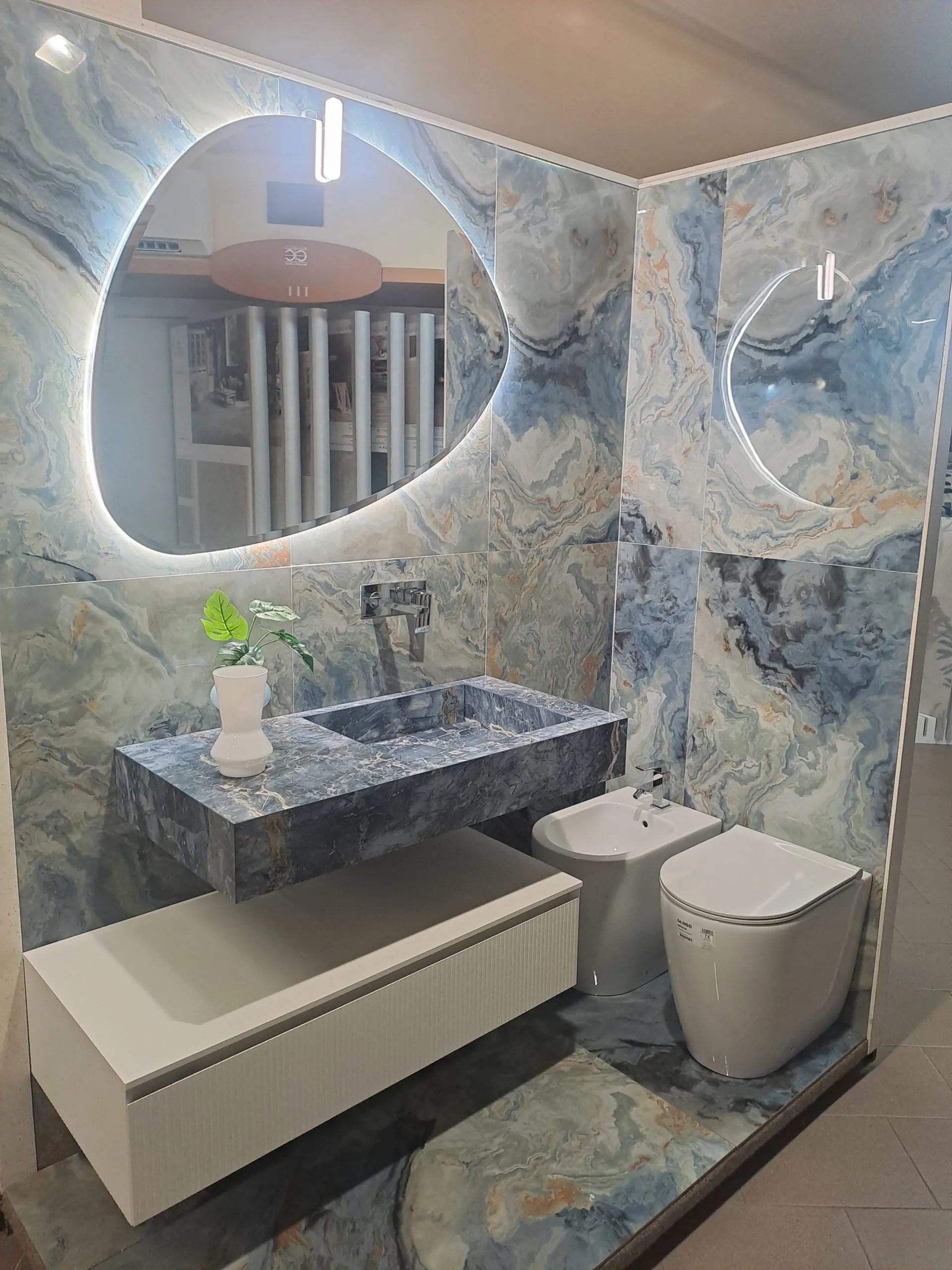 Ambiente bagno con grandi lastre effetto onice azzurro, lavabo monolitico e specchio retroilluminato dalla forma organica