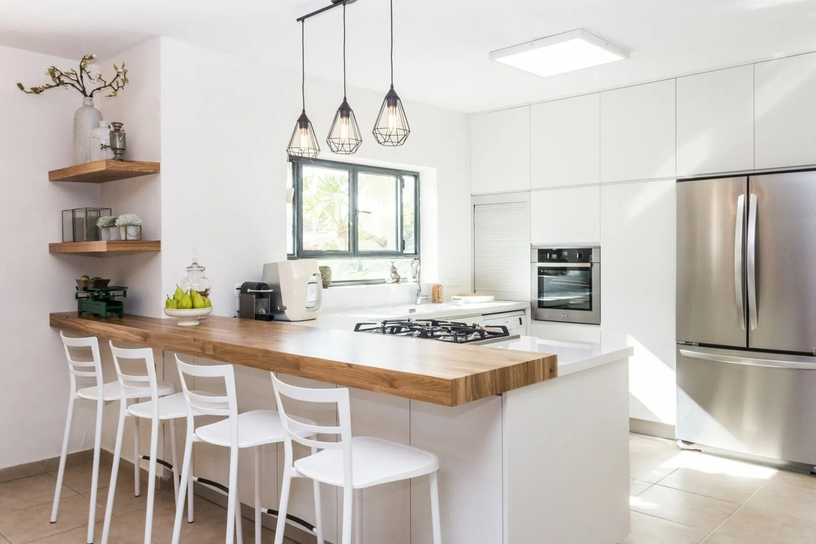 Cucina luminosa con penisola in legno, sgabelli bianchi e pensili chiari